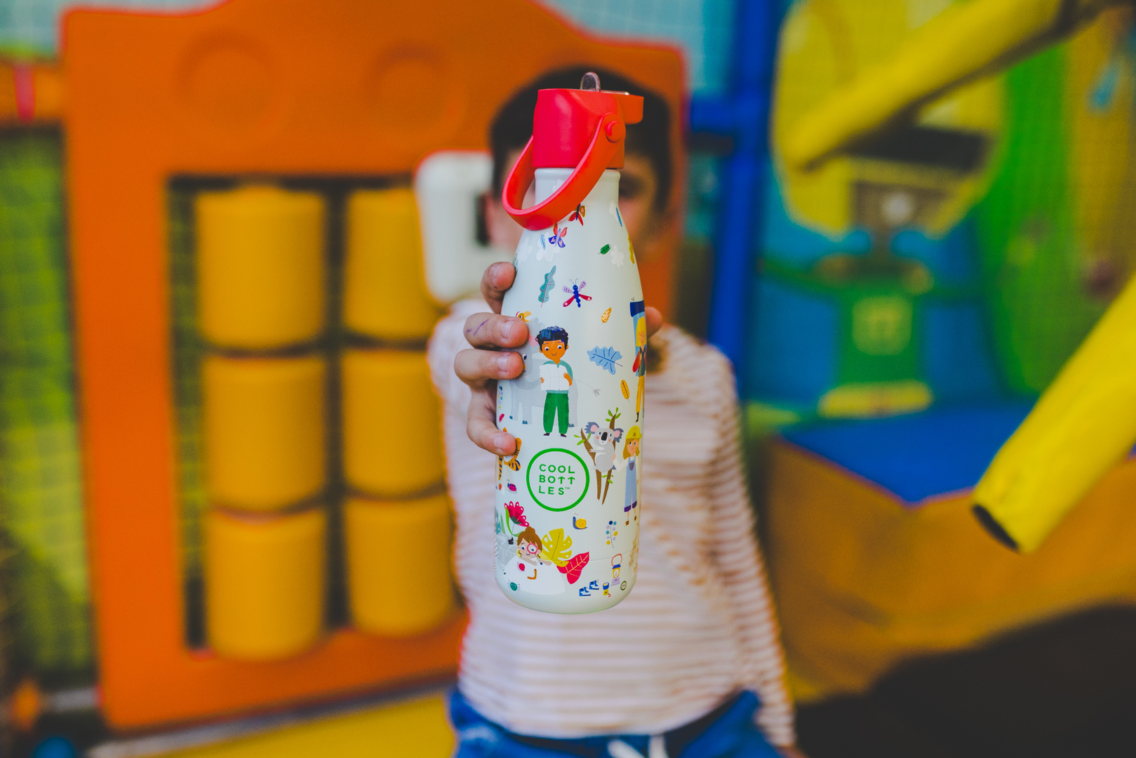 Dětská termo láhev Cool Bottles s růžovým sportovním víčkem v rukou dítěte v dětském centru.